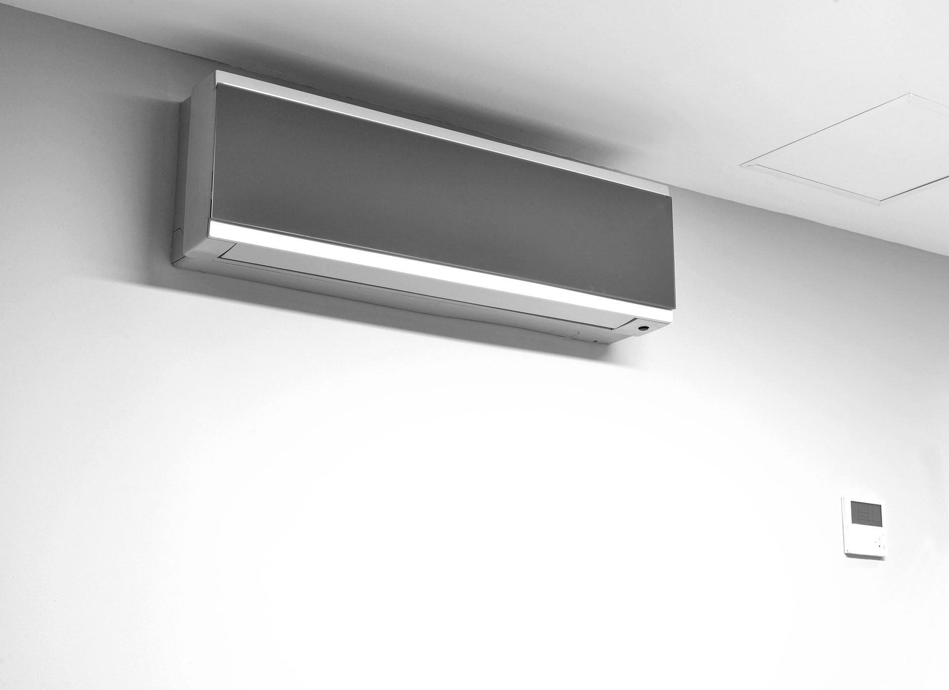 Unité intérieure murale de climatisation réversible gris anthracite au-dessus d’un thermostat